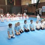 Dwa rzędy przedszkolaków siedzą w seiza na macie przed ceremonią zakończenia zawodów