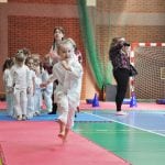 Dziewczynka w karategi biegnie po macie w konkurencji sprawnościowej, za nią kolejni uczestnicy czekający na start