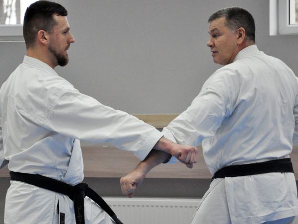 Dwaj karatecy z czarnymi pasami ćwiczą blok przedramieniem w zwarciu podczas seminarium