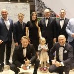 Grupa dorosłych w garniturach i sukniach wieczorowych oraz mała dziewczynka pozują do wspólnego zdjęcia w holu podczas Wejherowskiej Gali Sportu