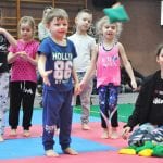 Grupka przedszkolaków w strojach sportowych stoi na macie w oczekiwaniu na start konkurencji