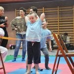 Dziewczynka przechodzi bokiem pod rozciągniętą taśmą w konkurencji zręcznościowej, obok stoją opiekunowie