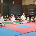 Dzieci i instruktorzy w karategi siedzą w seiza na macie podczas ceremonii zakończenia zawodów