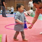 Instruktor podaje małemu dziecku hula-hoop podczas zabawy ruchowej na macie